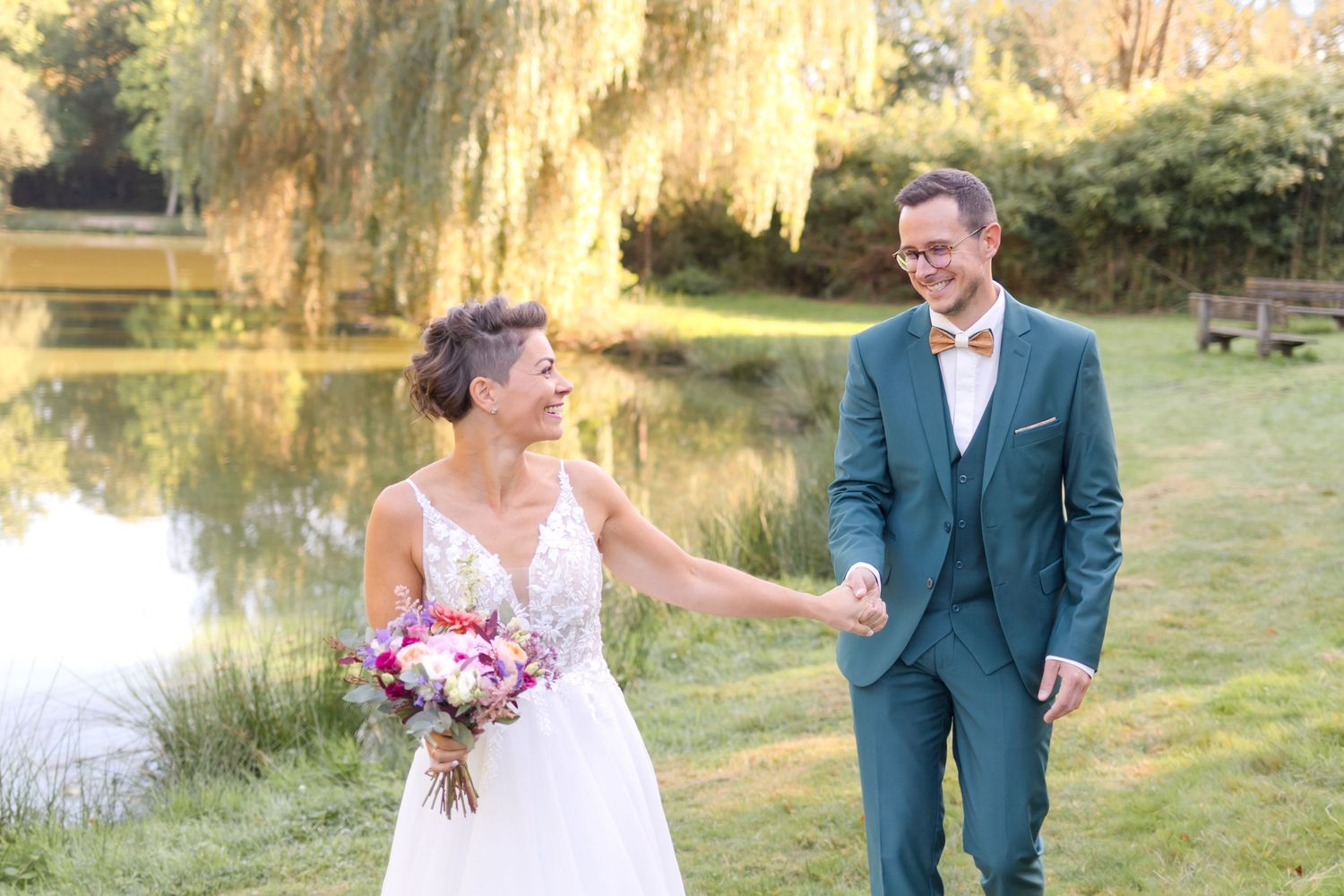 Wedding couple laughing together beside a pond with willow trees in the background.