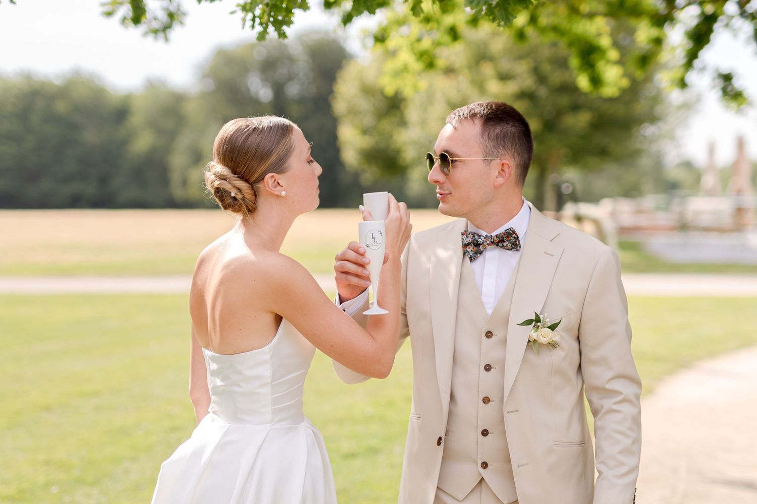 Wedding couple sharing drinks outdoors on sunny day.