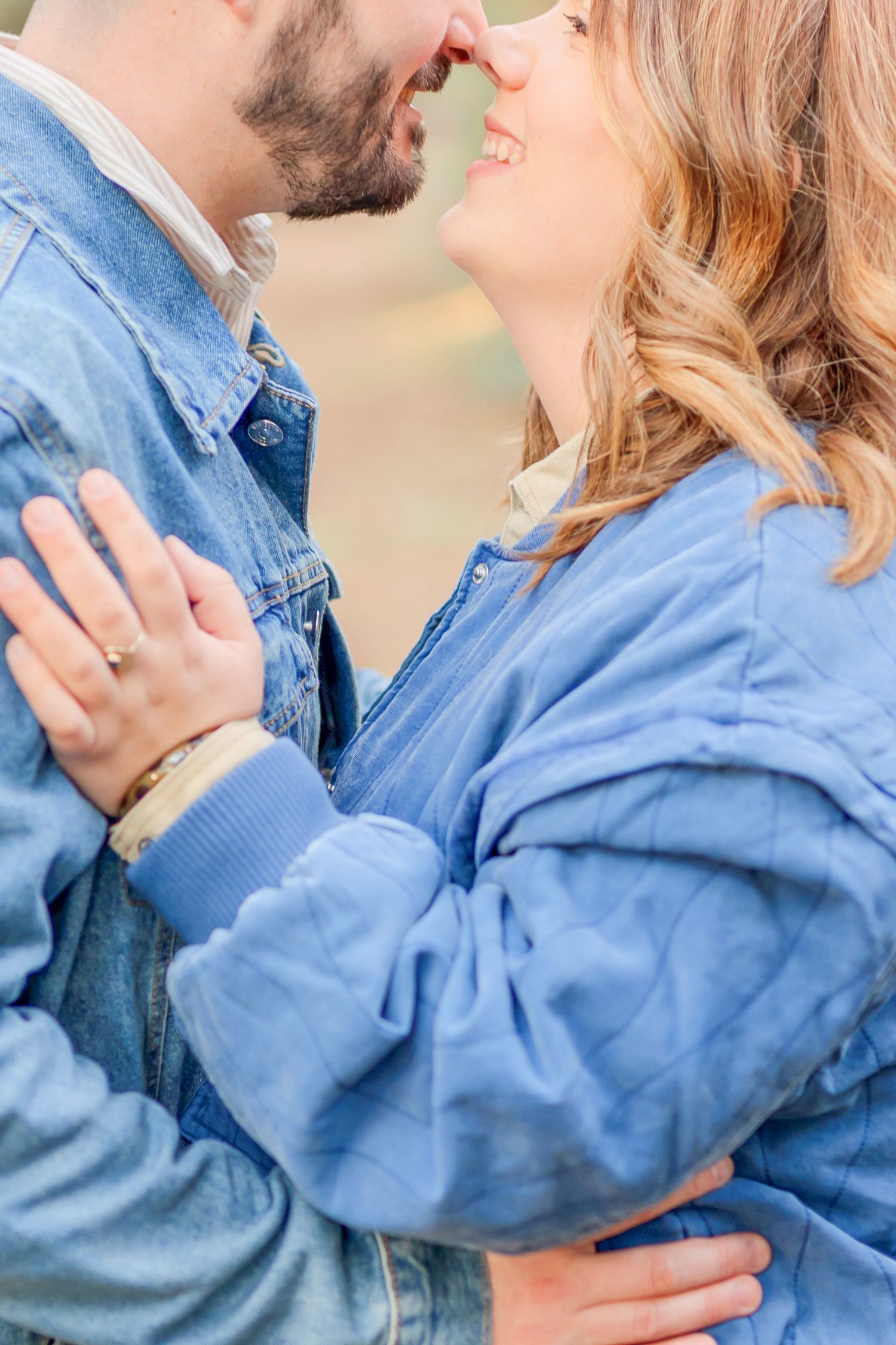 Close-up of couple in matching blue jackets sharing tender moment against autumn backdrop.