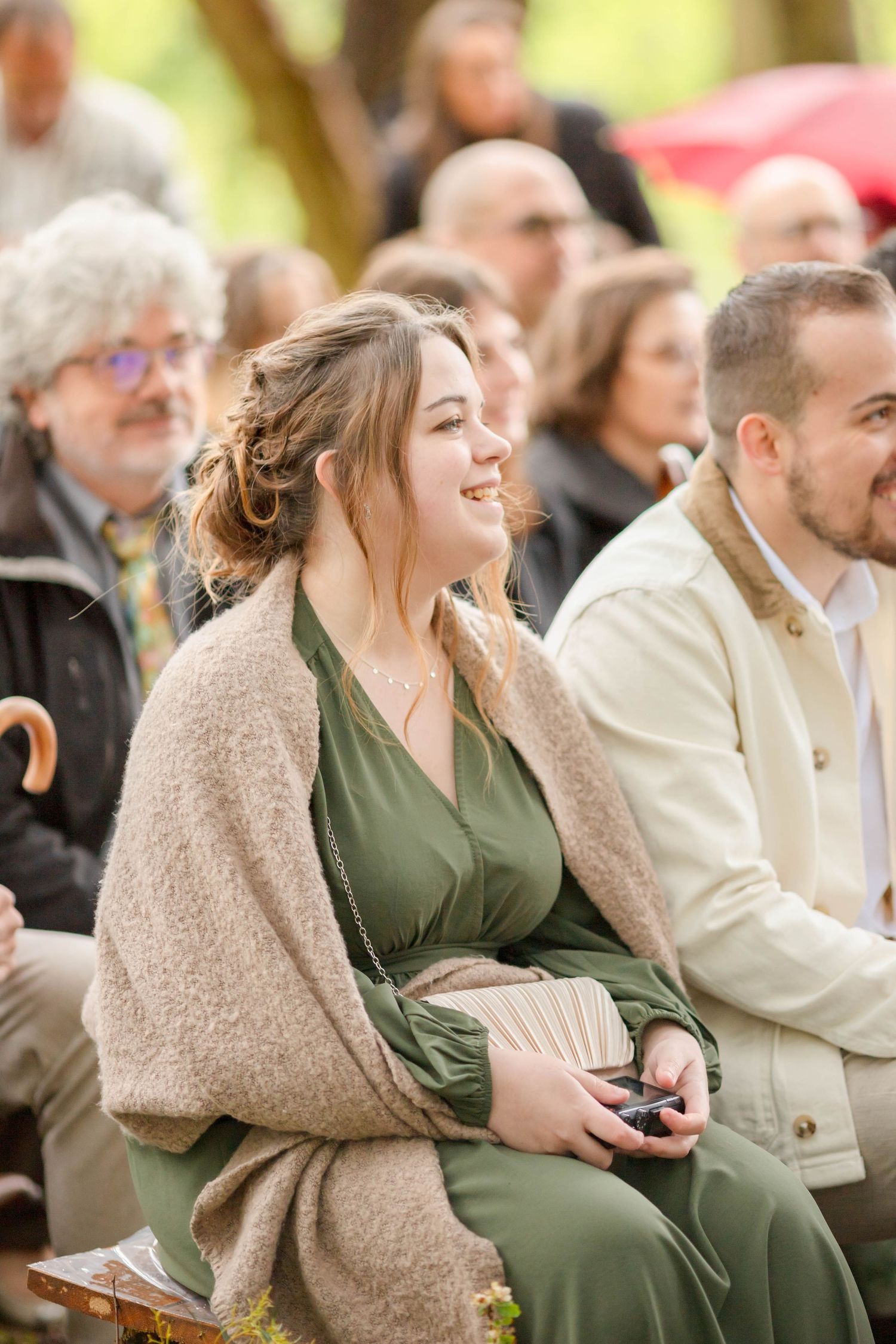 Wedding guests in warm clothing seated on wooden benches at an outdoor ceremony.
