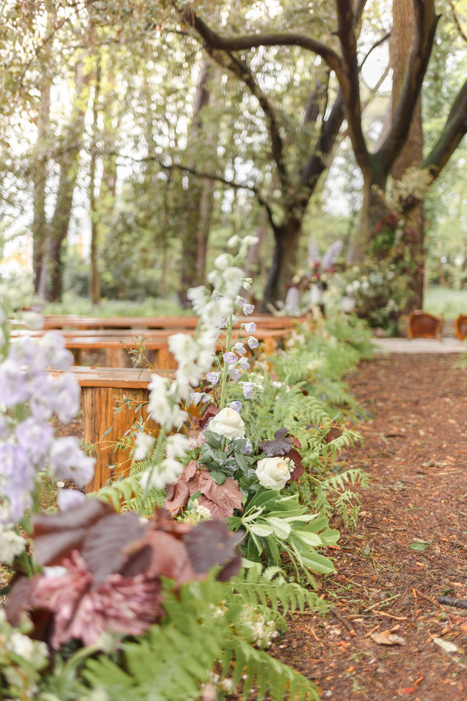 Outdoor woodland wedding ceremony setup with floral arrangements lining a rustic path.
