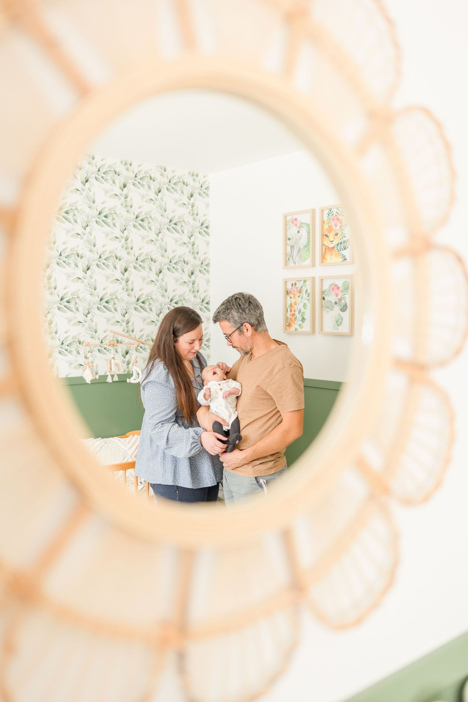 View through decorative mirror frame of nursery room with sage green walls and floral artwork.