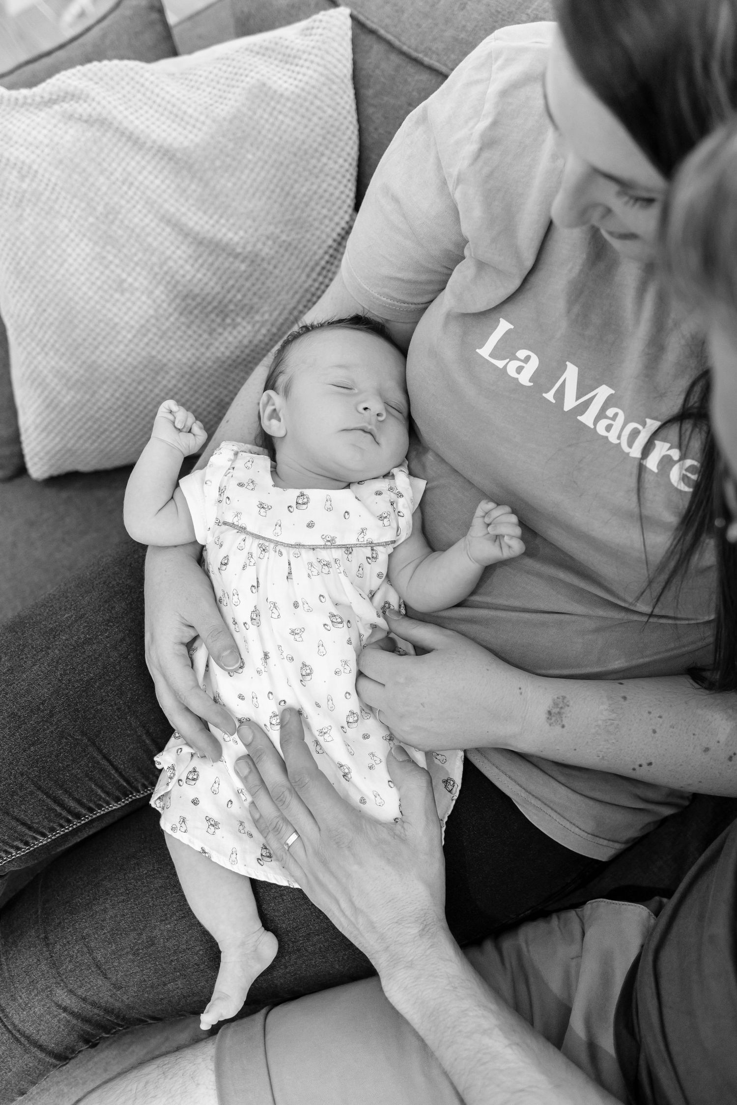 Black and white image of sleeping baby being cradled on couch.