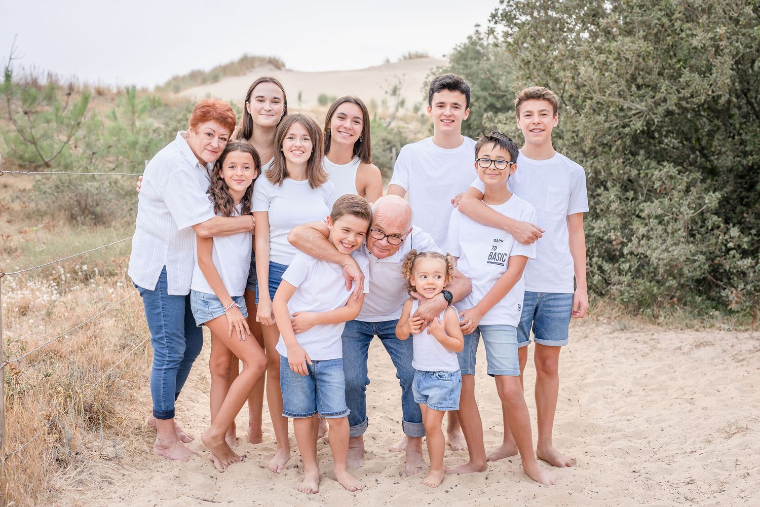 Extended family members in coordinated outfits gather for casual portrait on sandy trail.