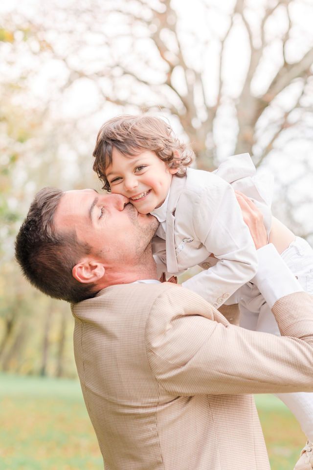 Sweet candid moment captured outdoors with autumn trees in soft focus background.