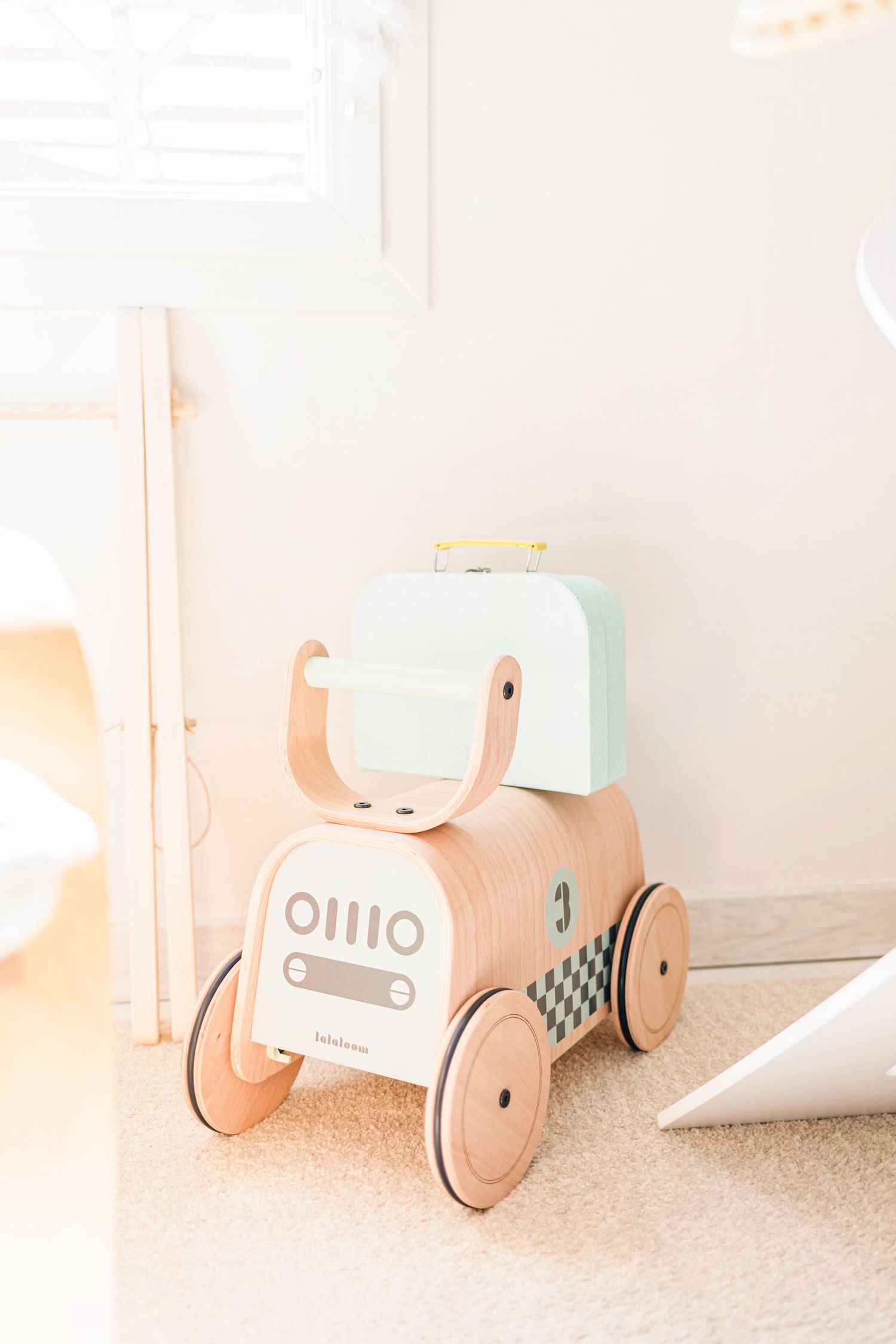 Wooden push cart toy with mint accents photographed on light carpet.