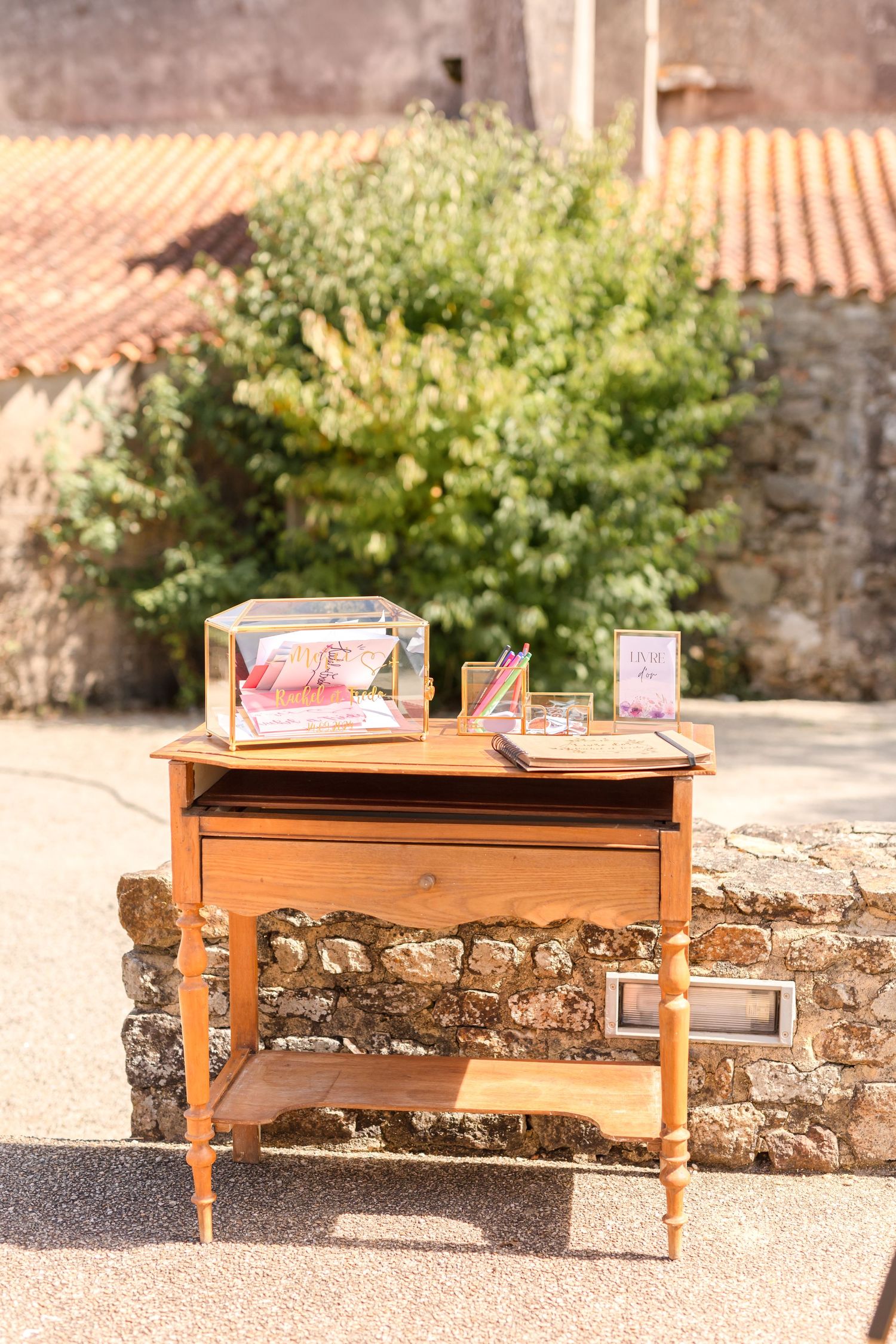 Vintage wooden side table decorated for wedding guest book display against stone wall.