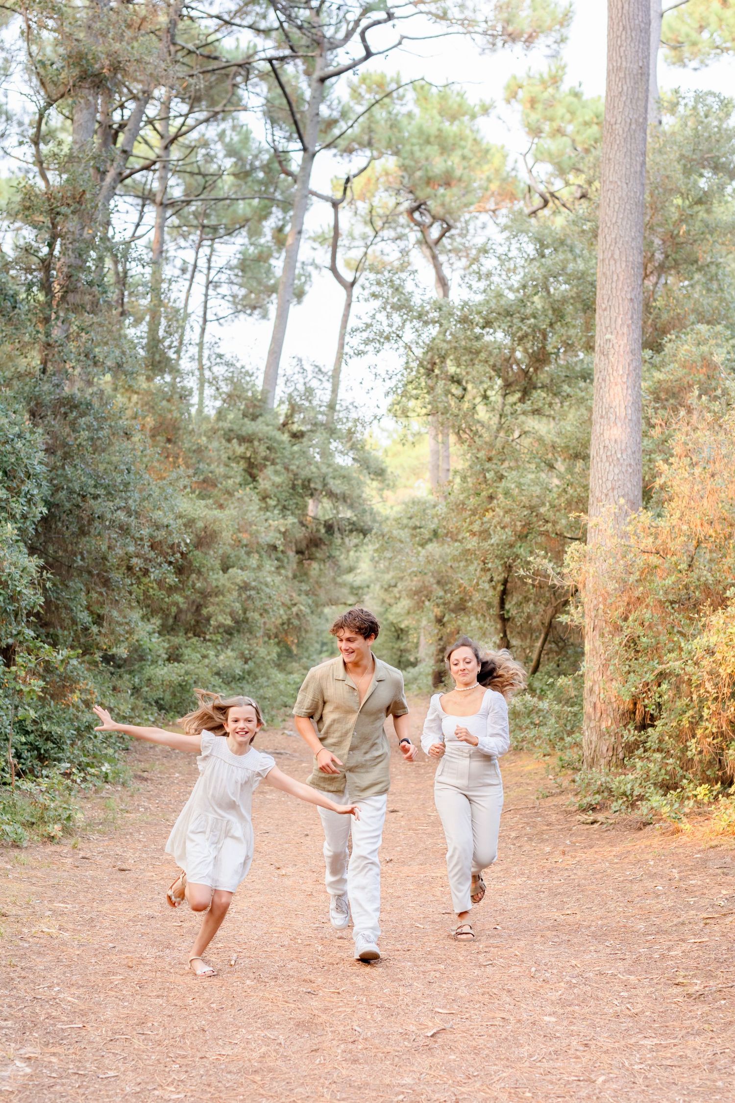 A family runs and plays together on a pine needle covered trail in matching outfits.