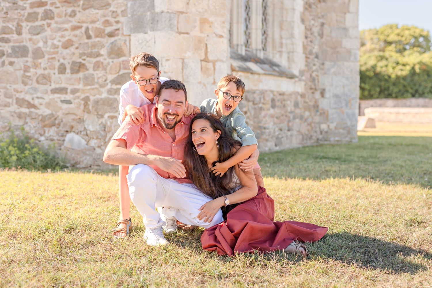Family members laughing together on grassy area by historic stone building.
