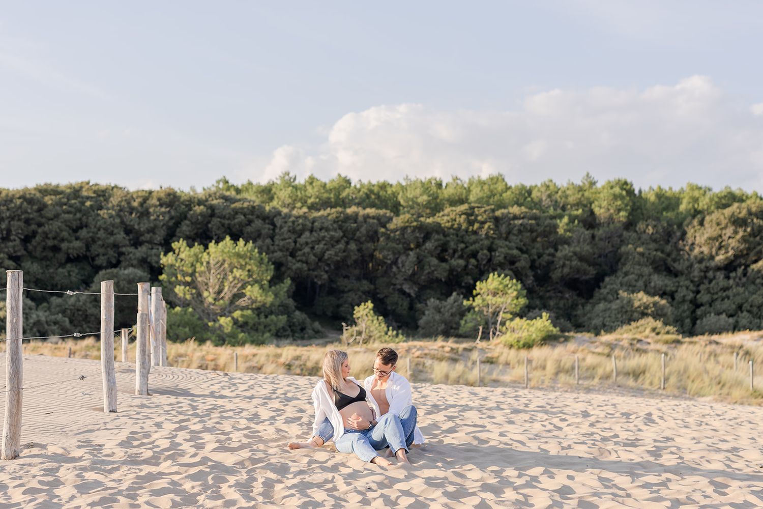 Sun-drenched beach with seagrass-dotted sand dunes and vacationers relaxing along the shoreline on a clear summer day.