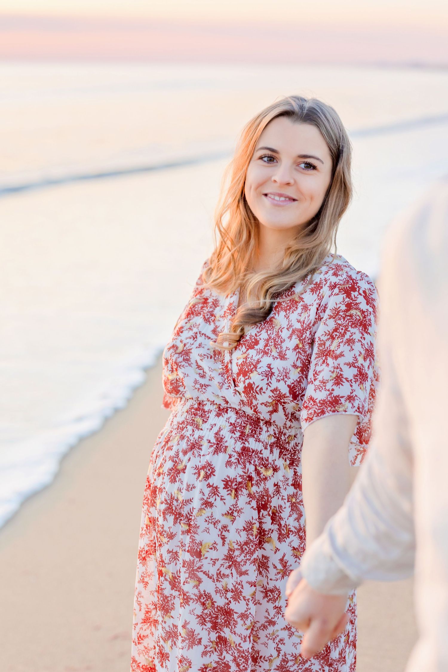 Couple laughing together on sandy beach at sunset wearing white and floral outfits.