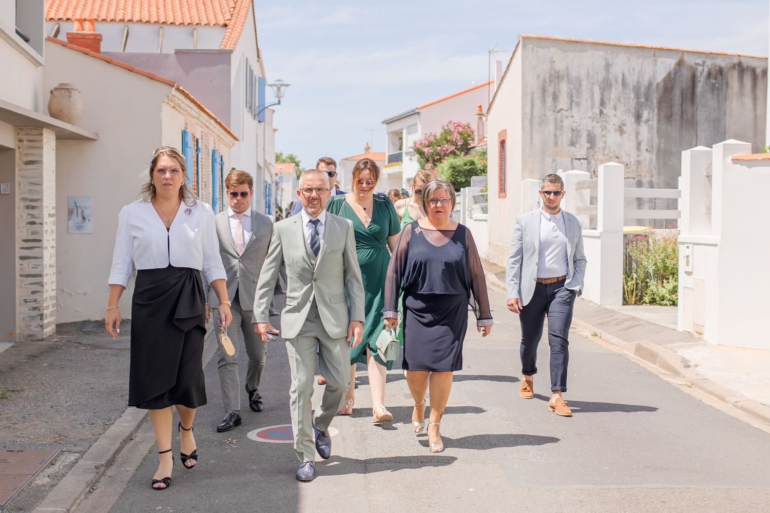 Wedding guests walking along a charming white-walled street with traditional architecture.
