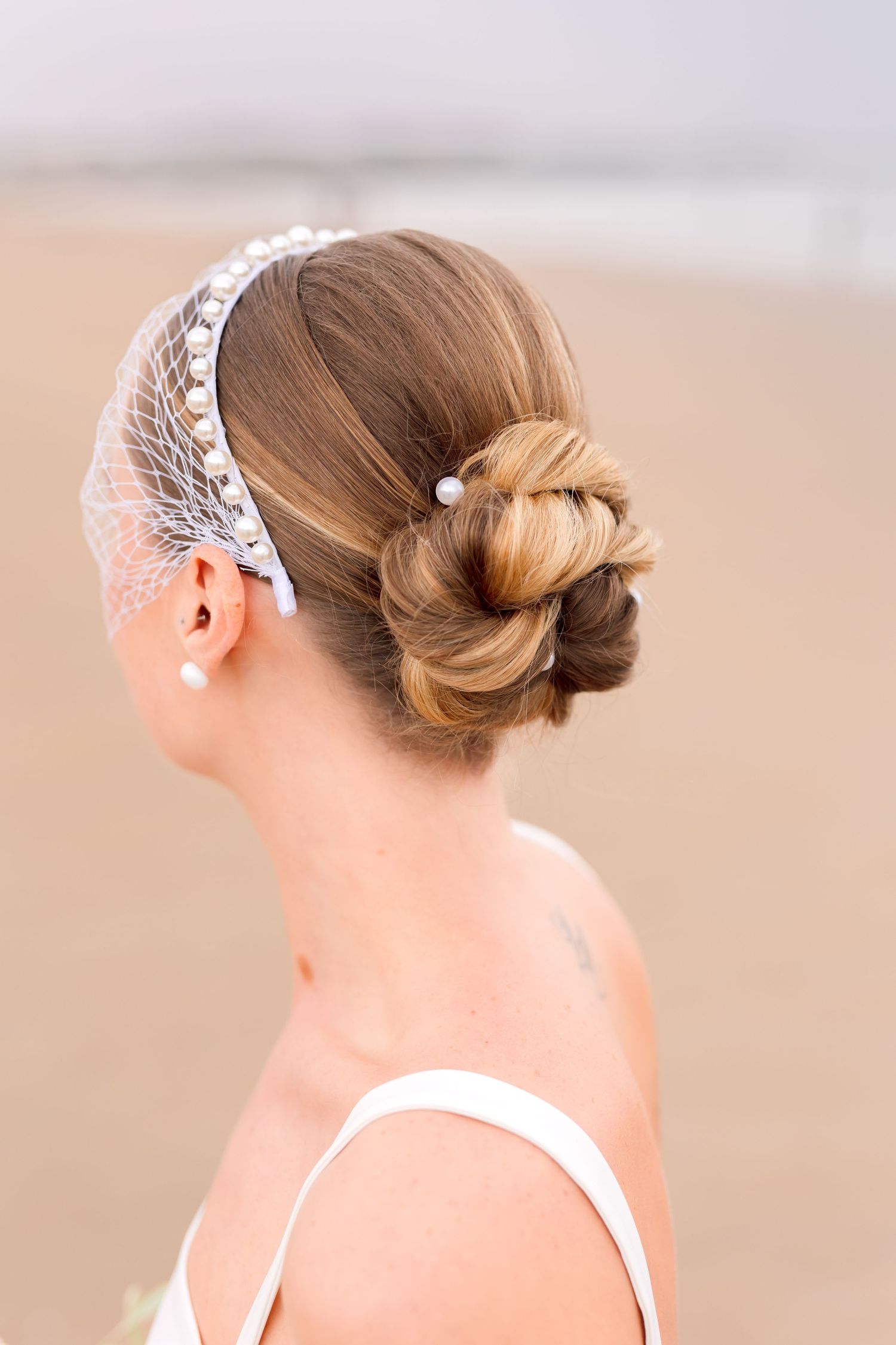 Elegant bridal hairstyle with ornate pearl headpiece shown from side profile on beach.