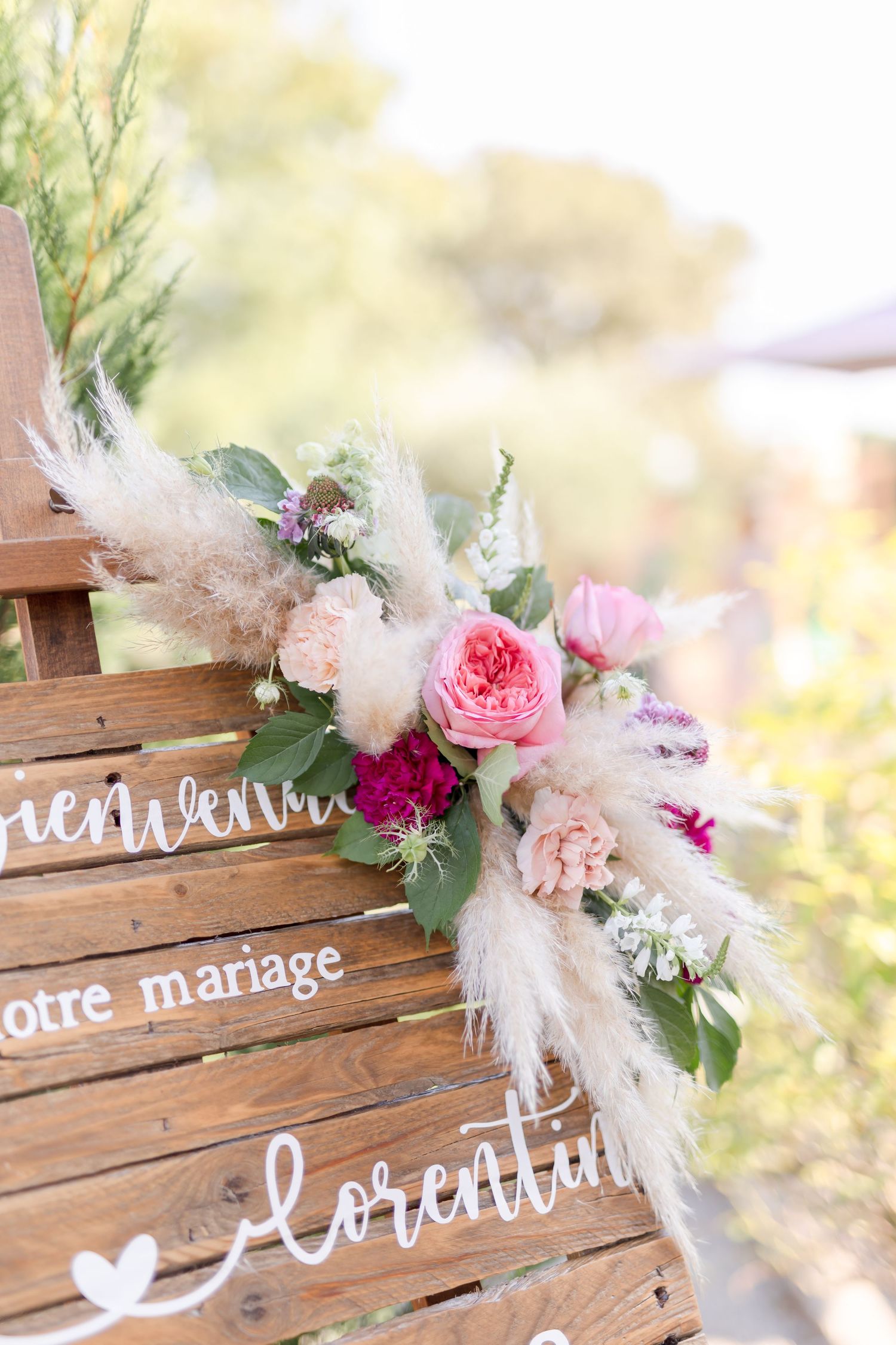 Wooden sign decorated with pink roses and pampas grass featuring French wedding text.
