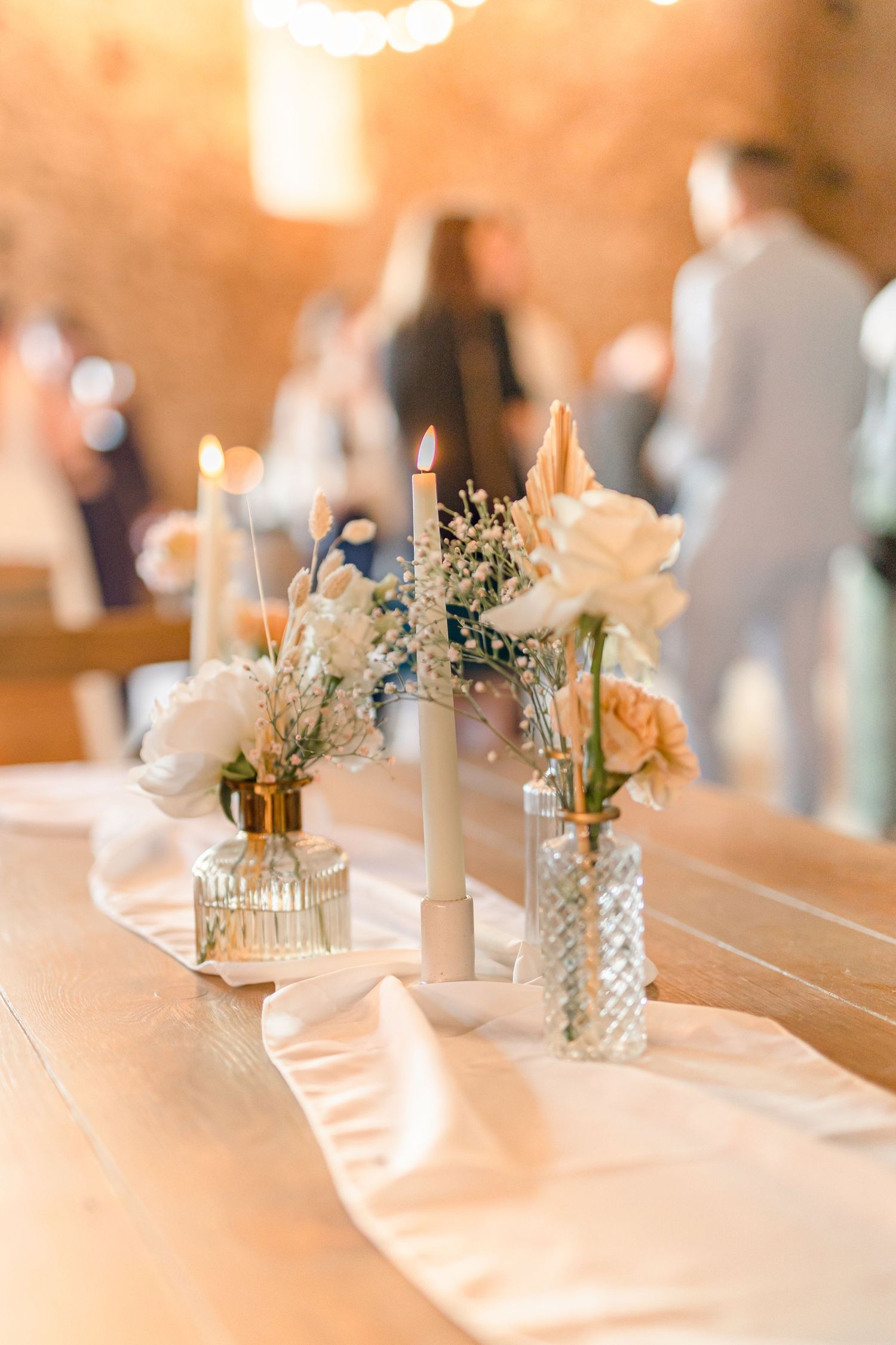 White floral centerpieces and candles line an elegantly decorated wedding reception table.
