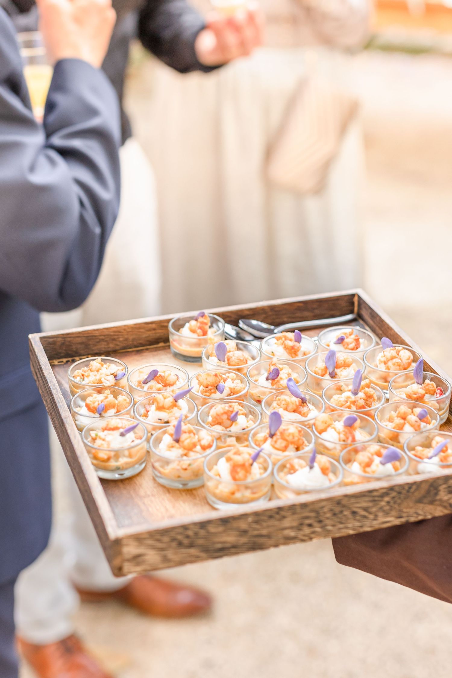 Elegant catering tray filled with appetizers in glass cups at outdoor event.