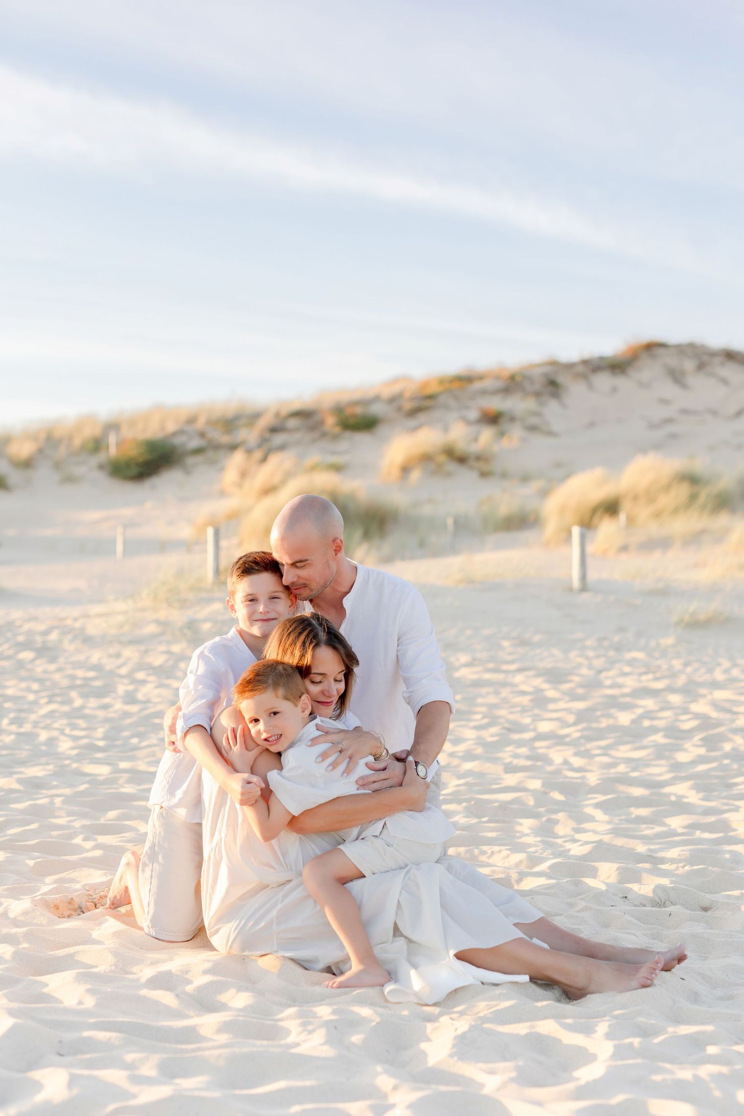 Tender family moment captured on beach with dunes in soft sunlight.