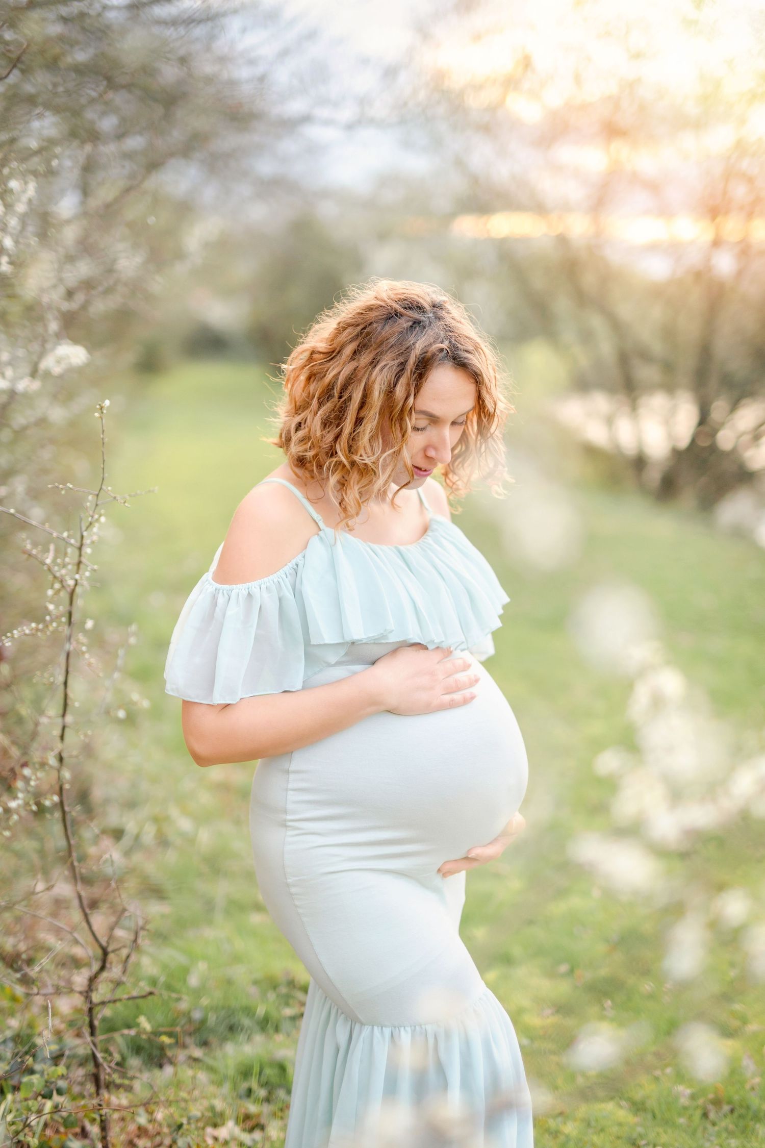 Delicate maternity portraits in a light blue dress against spring blossoms.