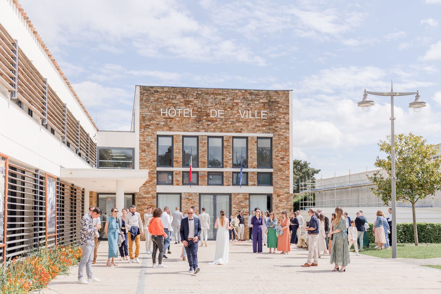 Wedding guests gather outside a historic brick building under blue skies.