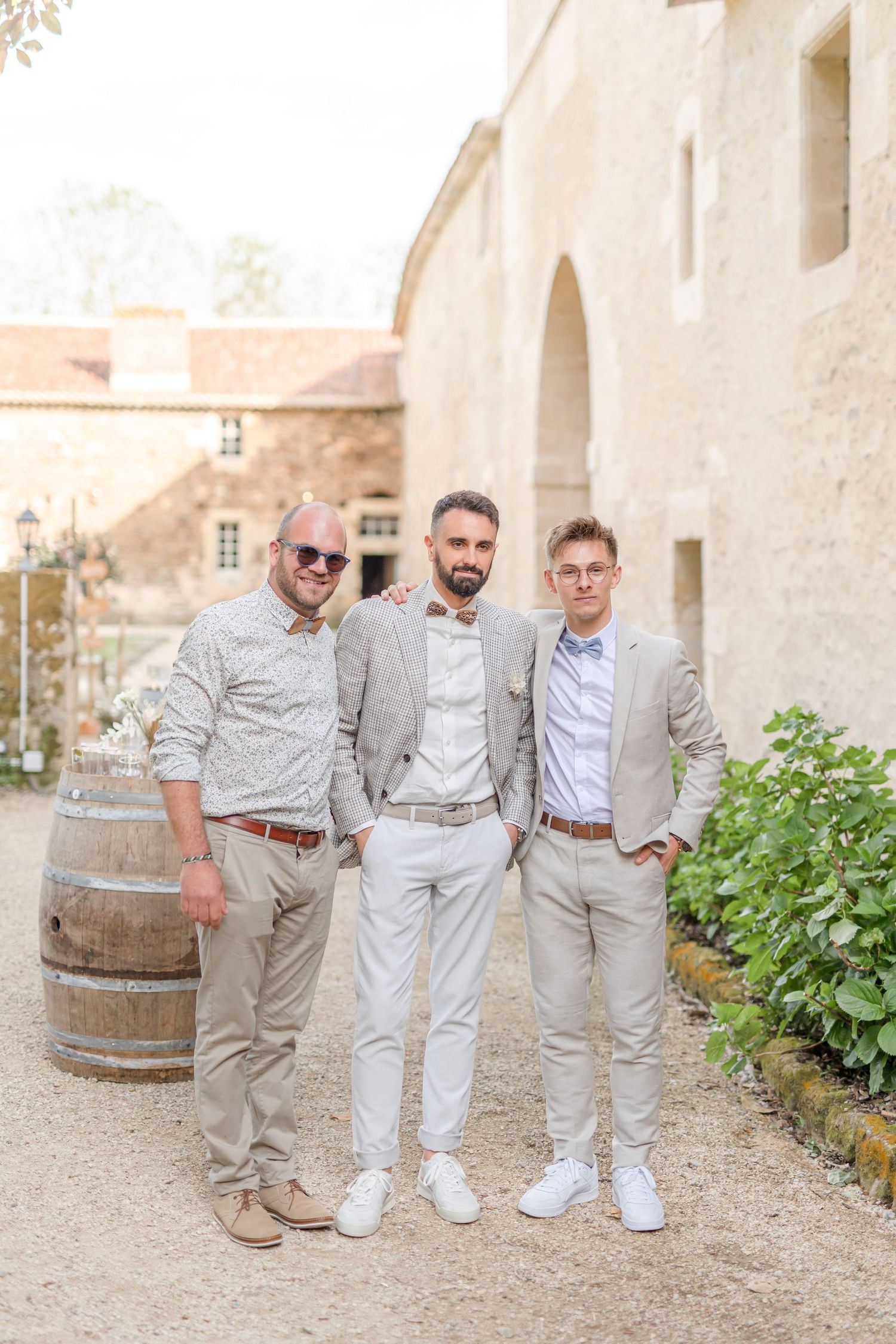 Wedding guests posing near rustic stone wall and wine barrel at outdoor venue.