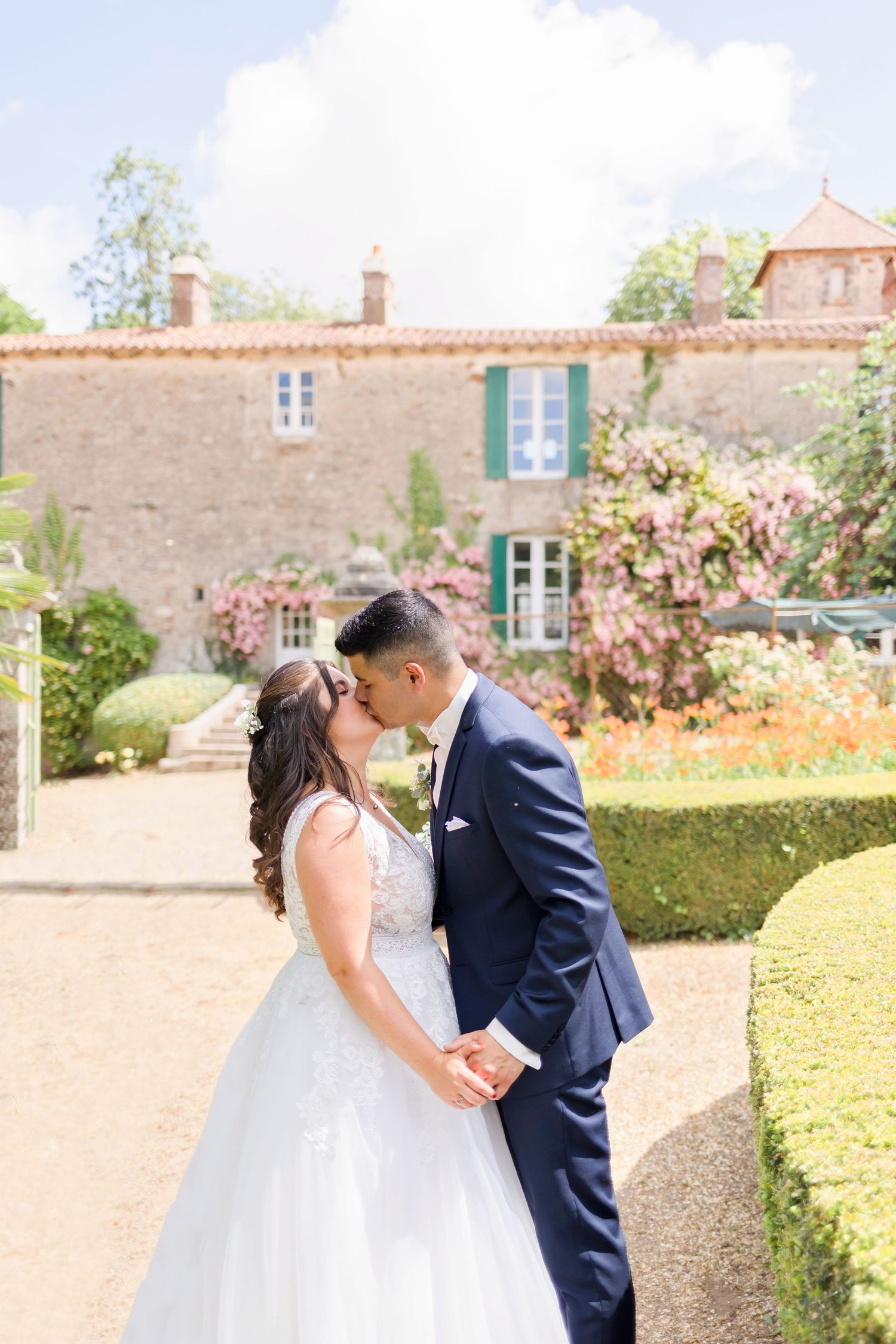 A wedding couple shares an intimate moment in front of a rustic stone mansion with green shutters.