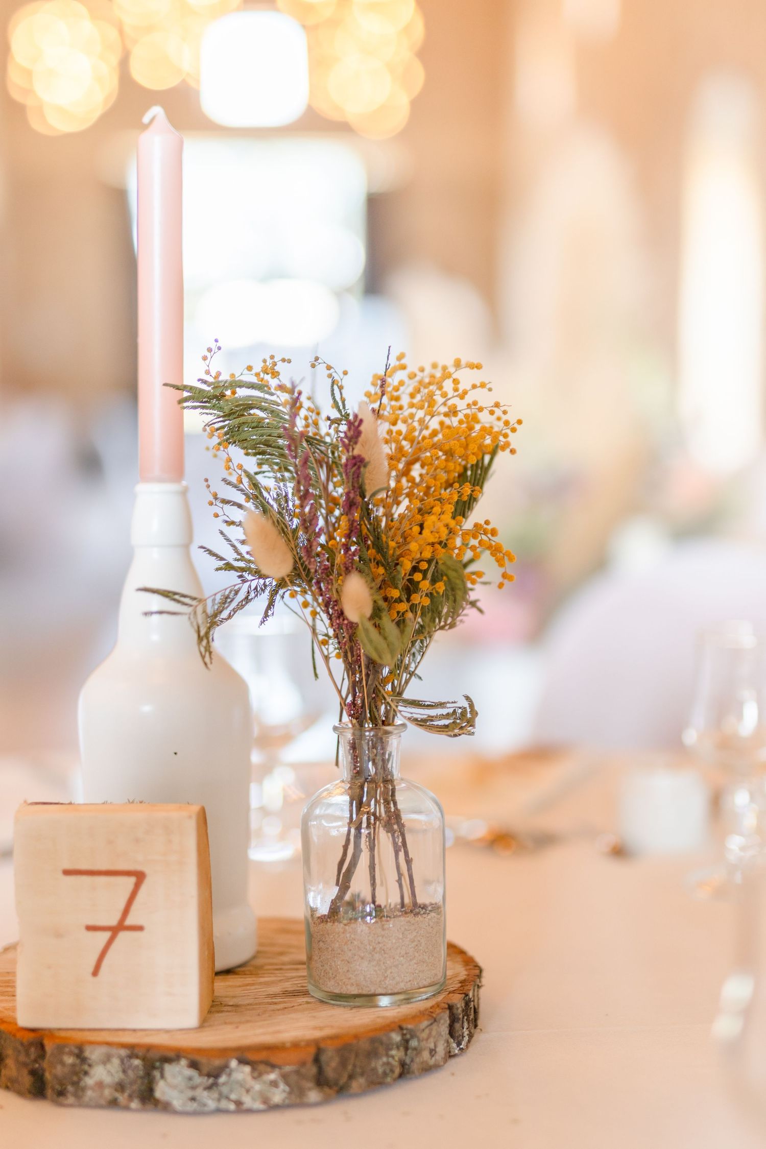White ceramic vases with dried flowers on wooden slices as rustic table centerpieces.