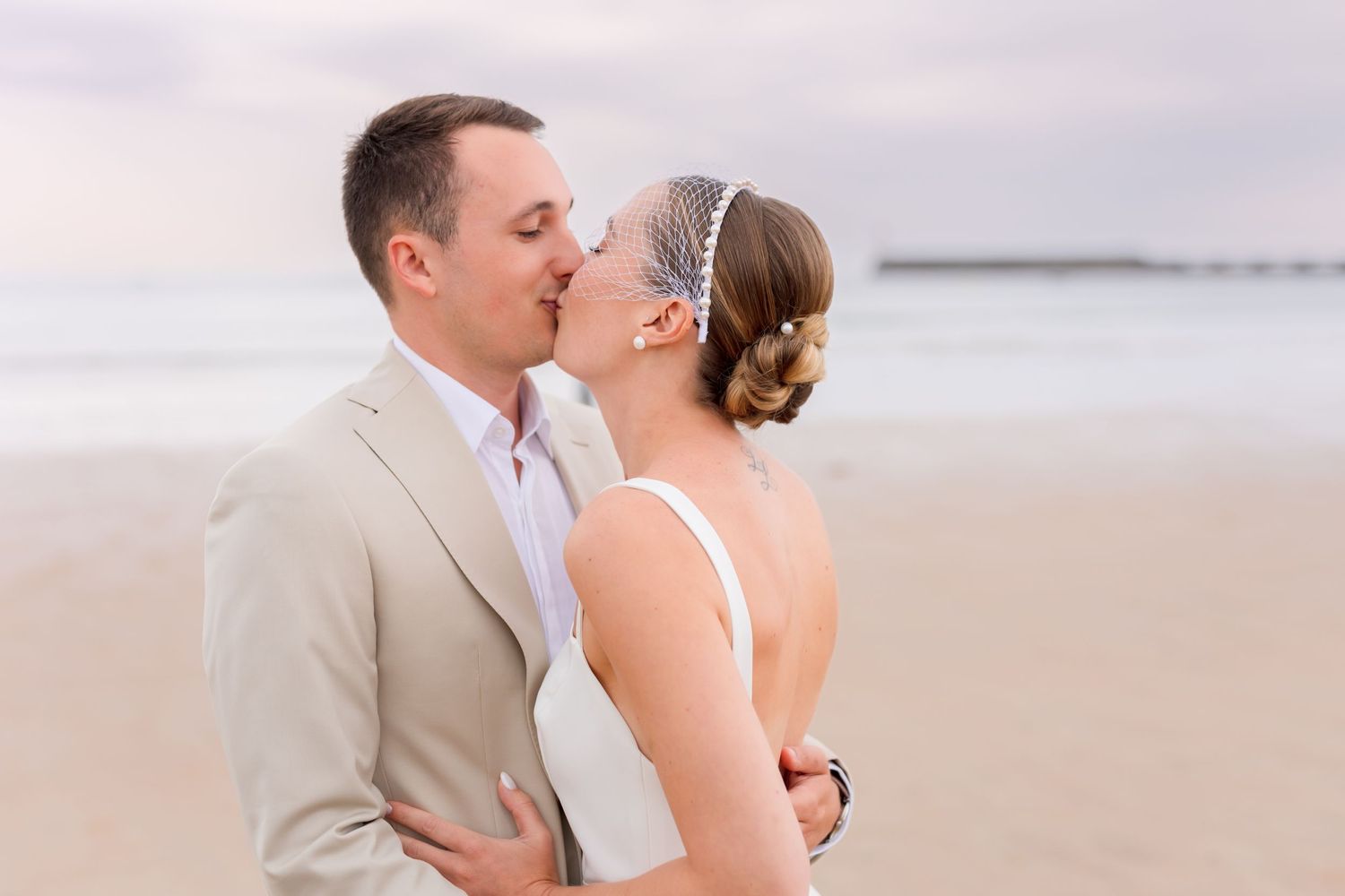 Romantic beach wedding portrait with couple in beige suit and white dress sharing a tender moment.