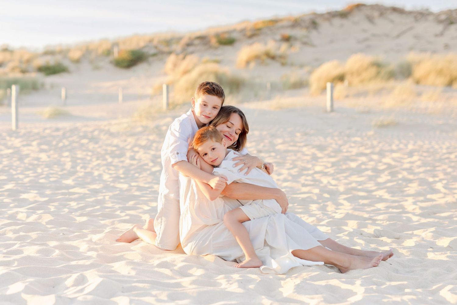 Family sharing embrace while sitting on sandy beach during sunset.