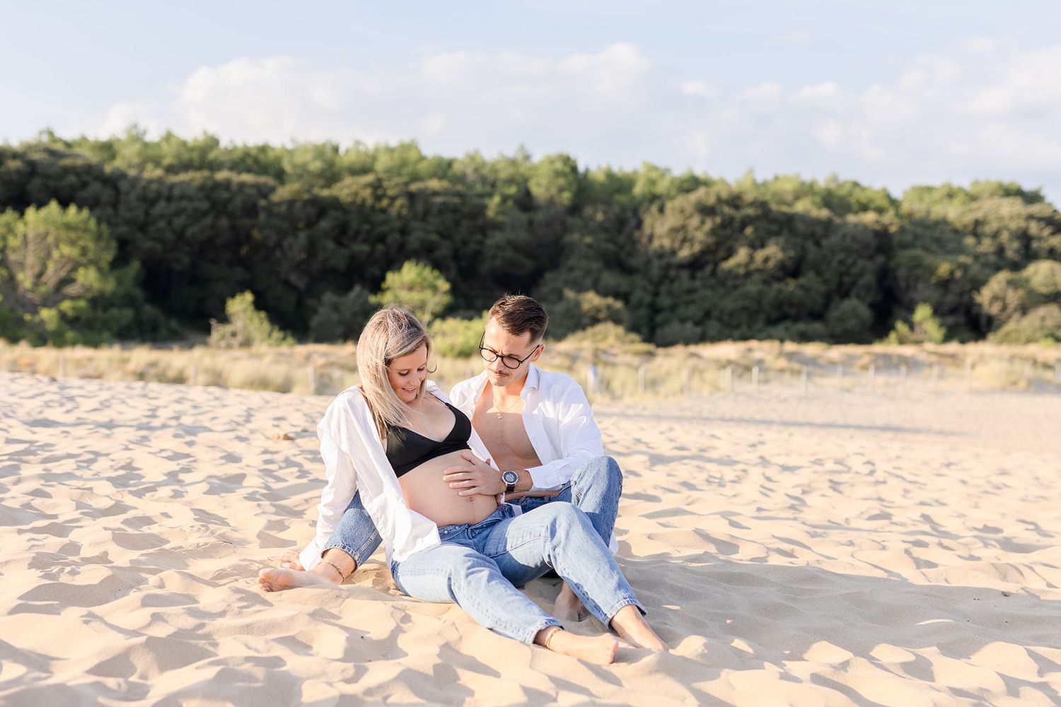 A couple sits intimately together on a sandy beach during sunset showing affection and romance.