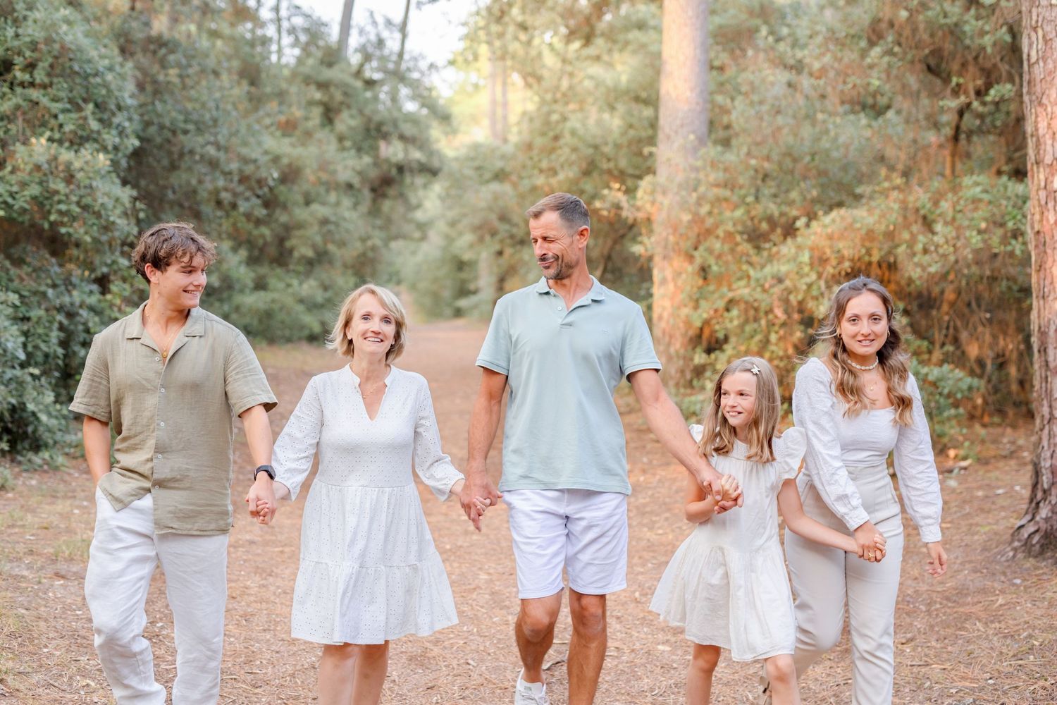 A family in coordinated white and beige outfits poses for photos on a wooded trail.