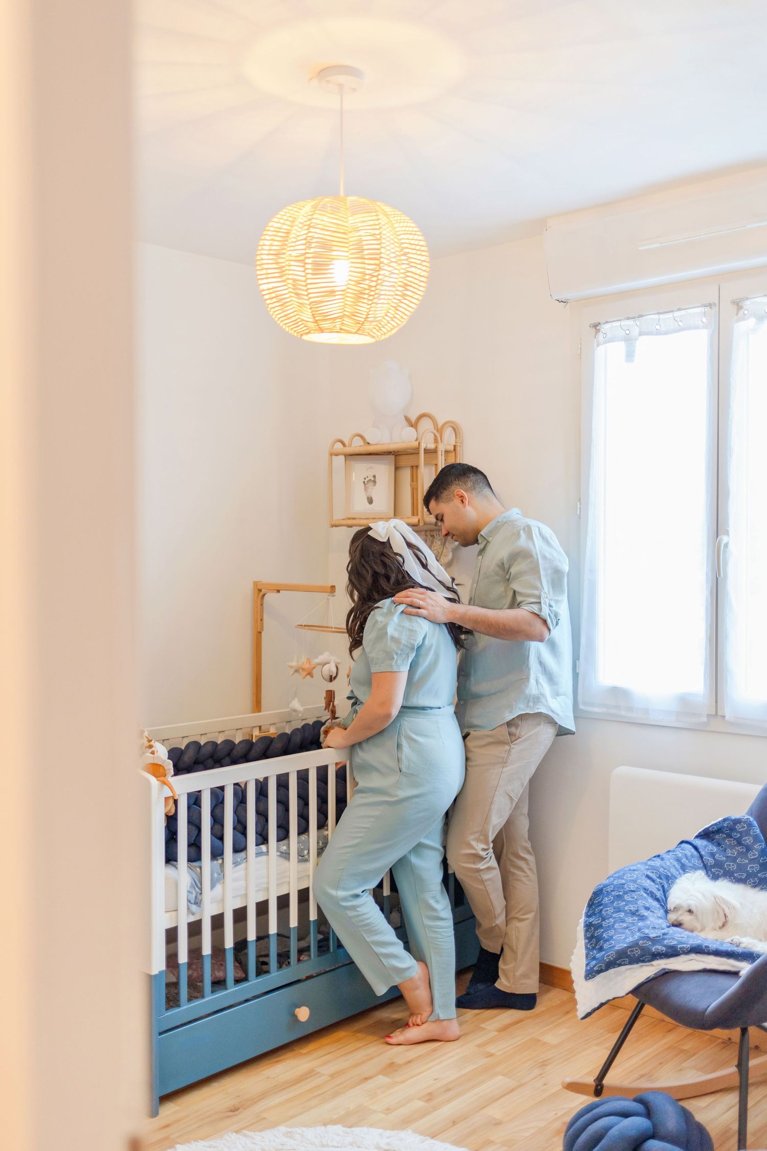 Modern nursery interior with woven pendant light, crib, and family moment.