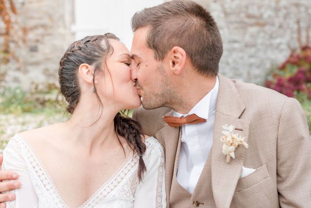 Intimate wedding portrait against weathered stone wall with delicate floral boutonniere.