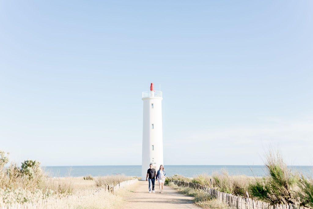 Distant view of lighthouse with people walking along coastal path.