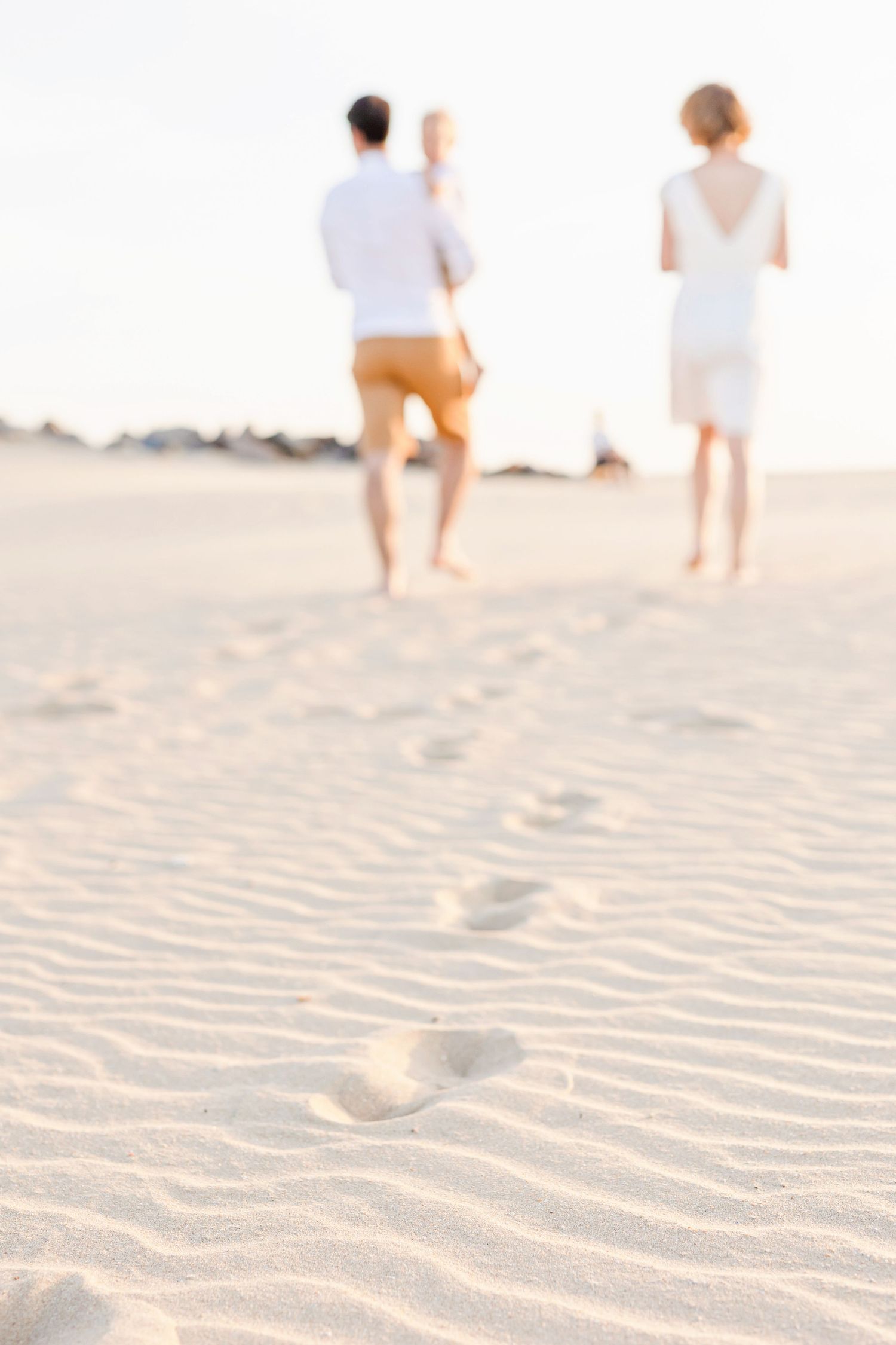 Sandy beach footprints with figures walking in soft focus during golden hour.