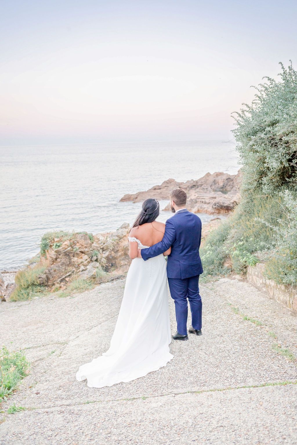 A couple walks along a scenic coastal path with white flowers and ocean views.