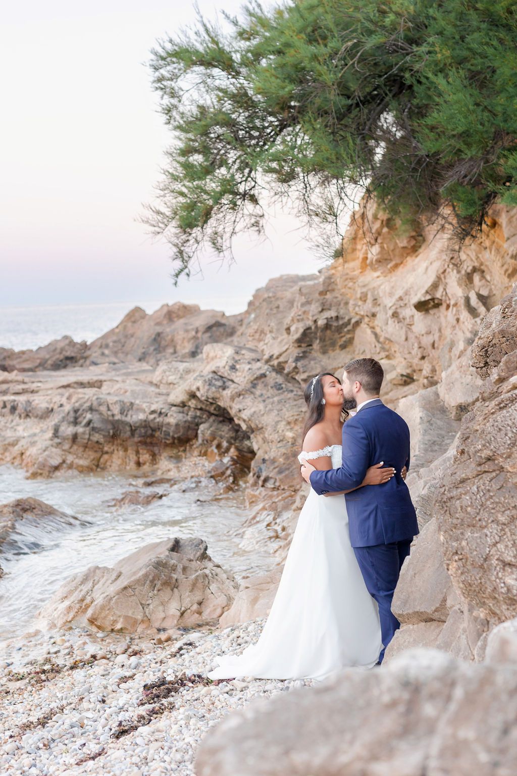 Romantic wedding portrait against rugged coastal cliffs and evergreen trees.