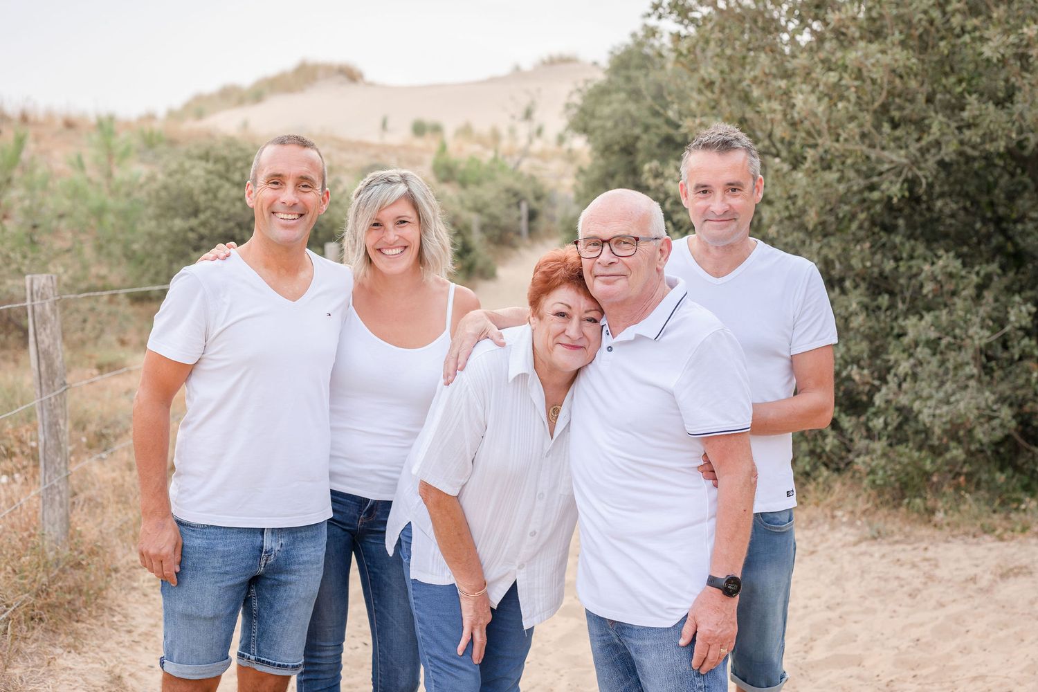 Small family group in coordinated white tops and denim poses on natural path.