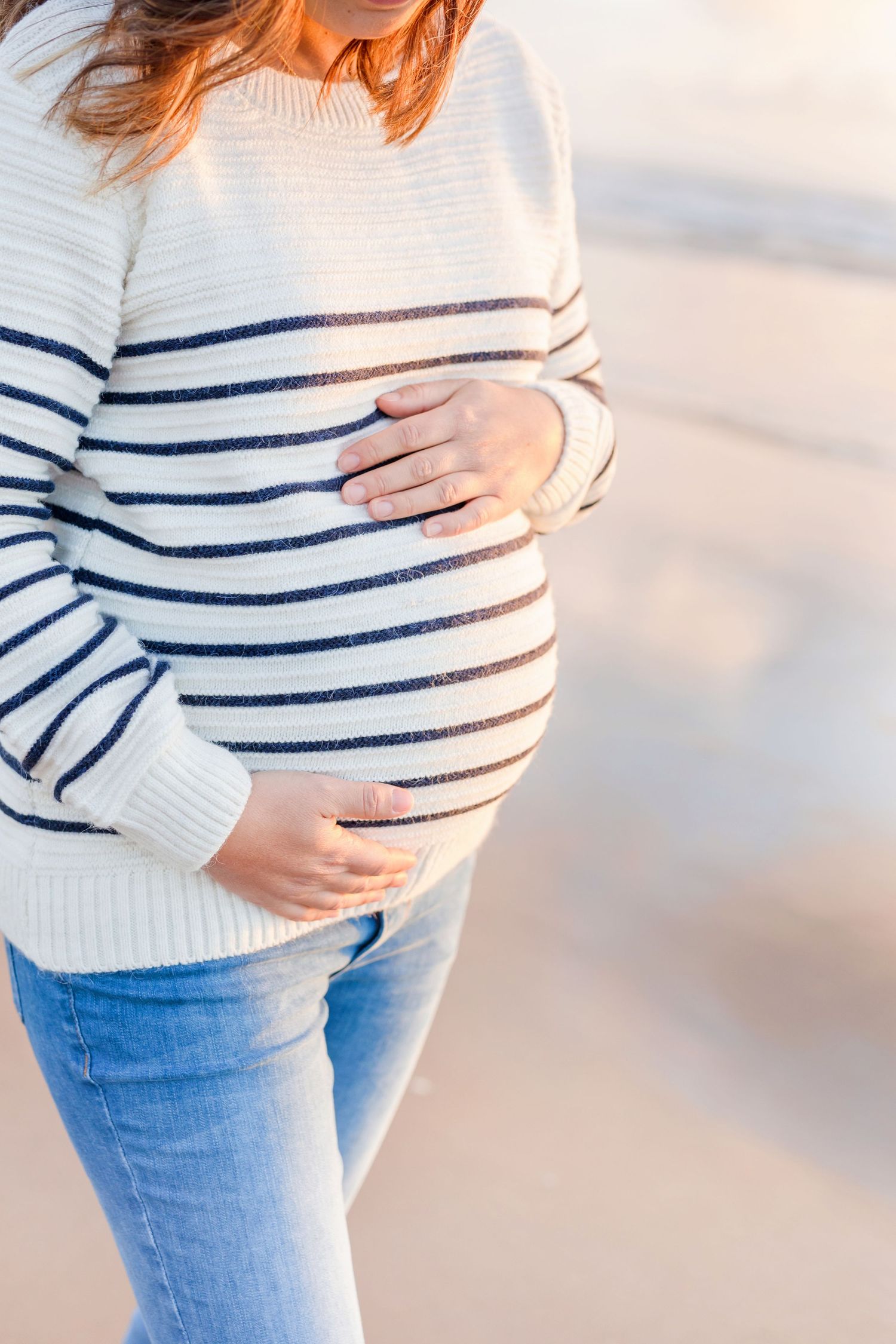 Close-up shots of pregnant belly in white and navy striped sweater against sunset background.