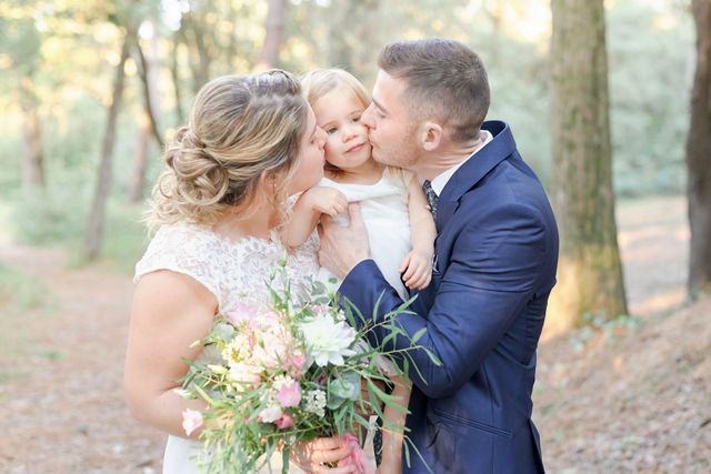 Wedding photograph outdoors in wooded setting with romantic moment and floral bouquet.