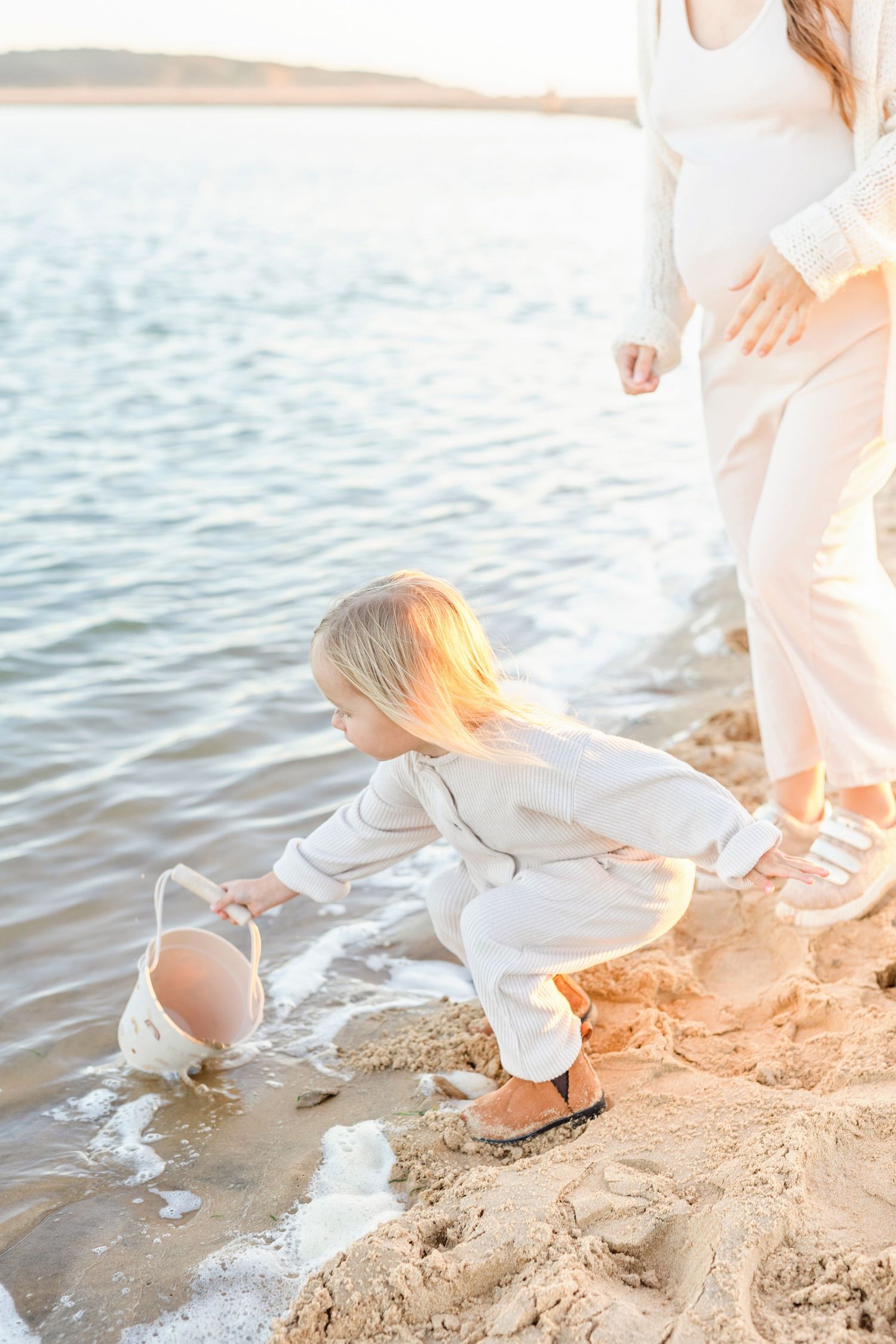 A small child plays in wet sand at the beach during golden hour.