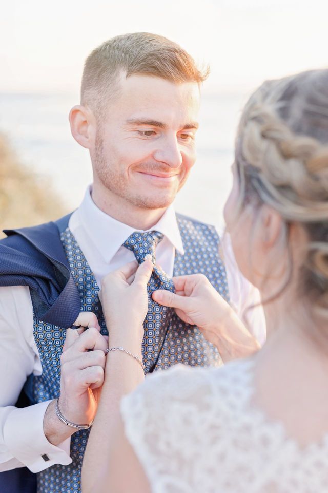 Close-up of wedding couple adjusting the groom's tie on the beach.