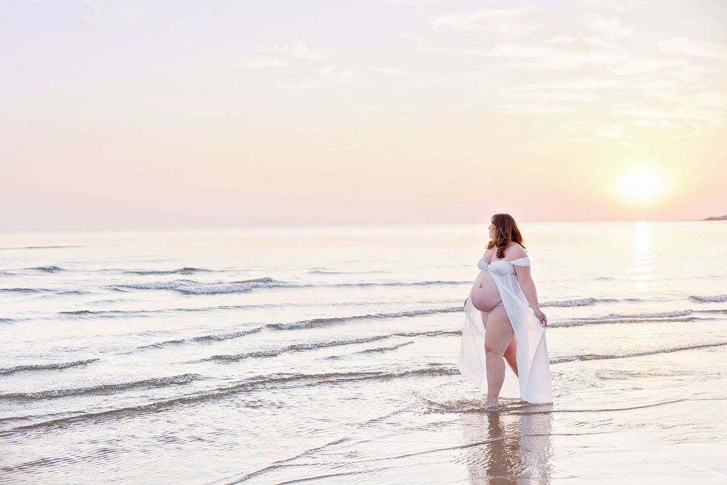 Silhouette of person in white dress walking along beach at golden sunset.