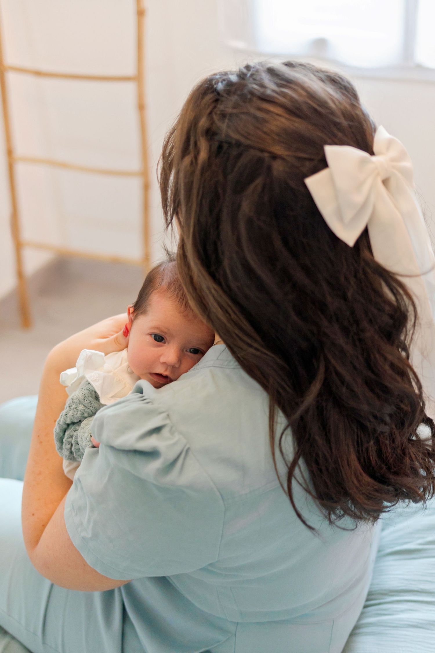 Mother in mint dress holding sleeping baby against her shoulder.