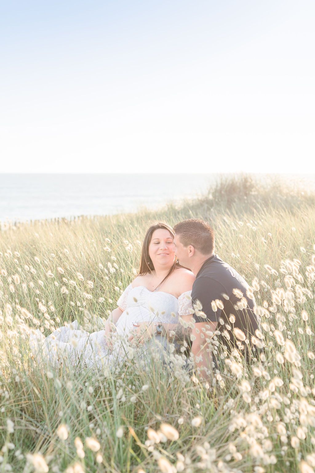 A romantic couple embraces in a field of white wildflowers at sunset.