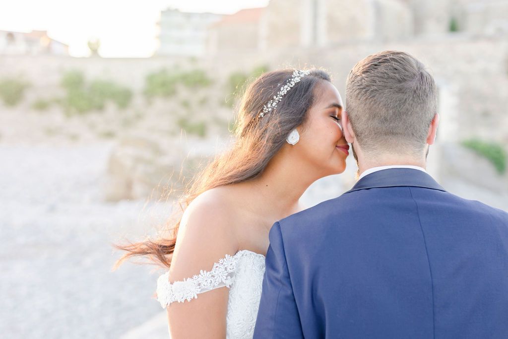 Tender wedding moment captured against blurred architectural background in warm light.