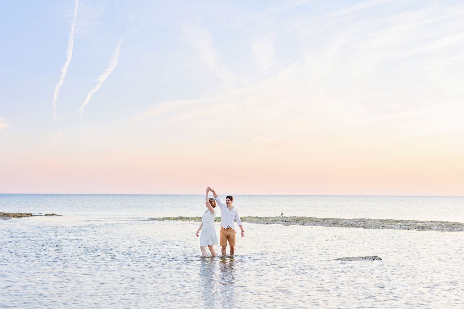 Two figures stand together in calm ocean waters during a dreamy sunset beach session.
