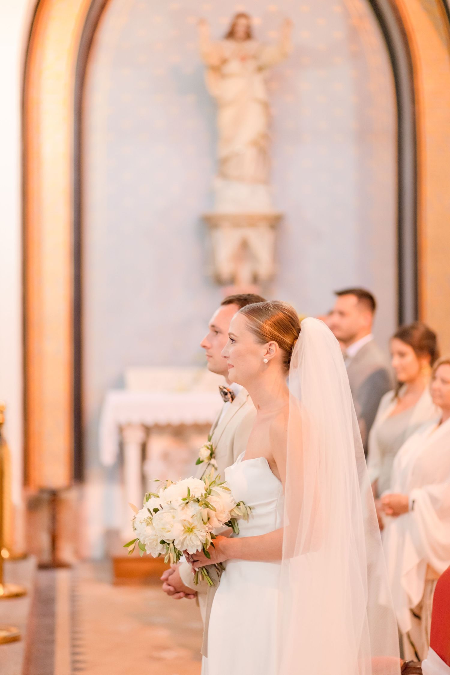 A bride holds a white bouquet during a traditional church wedding ceremony.