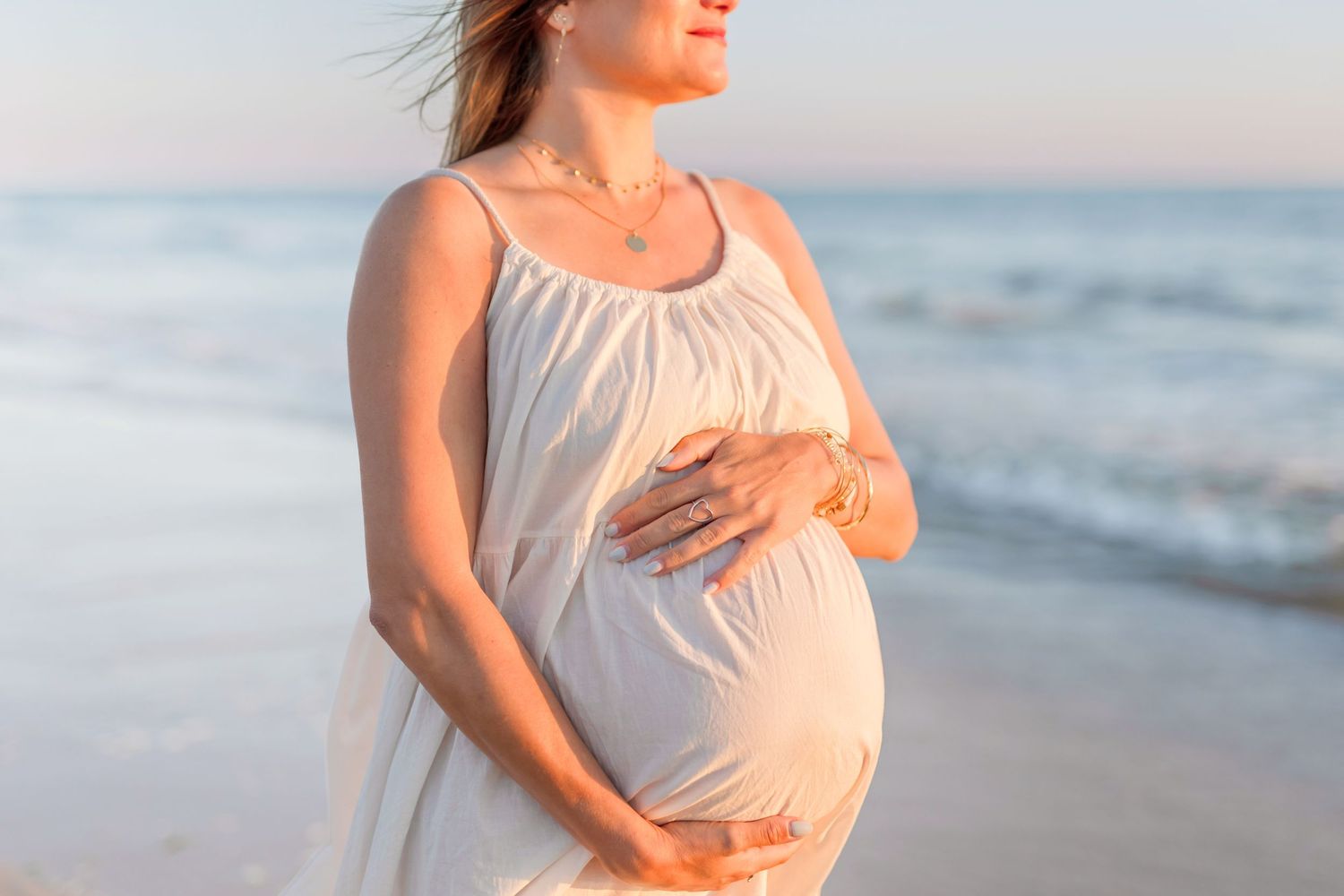 White flowy maternity dress highlighted against sunset beach backdrop.