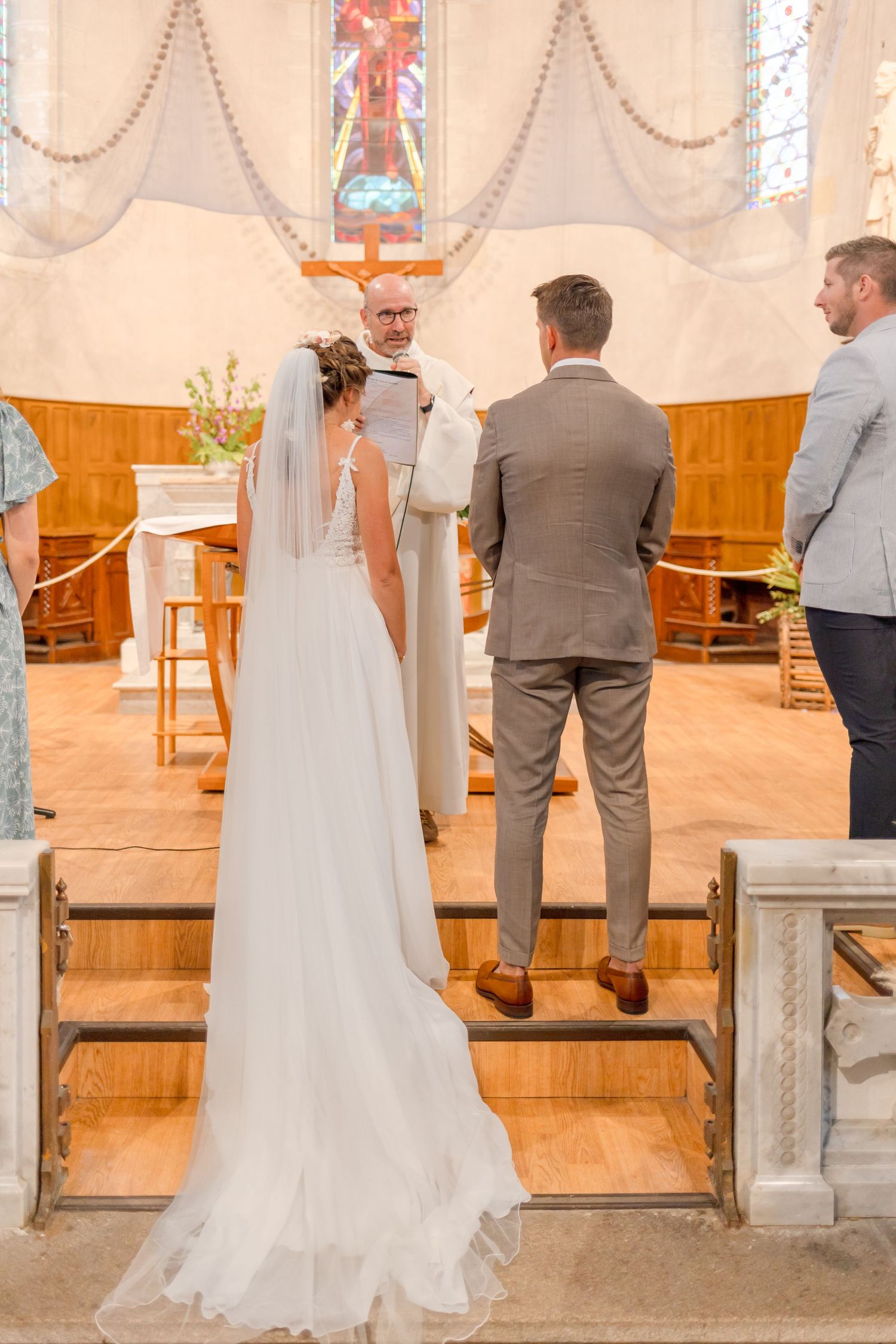 Wedding couple stands at altar during church ceremony with decorative lighting.