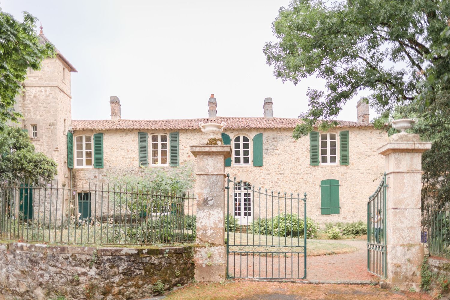 Stone facade of a rustic French country estate with green shuttered windows and iron gates.